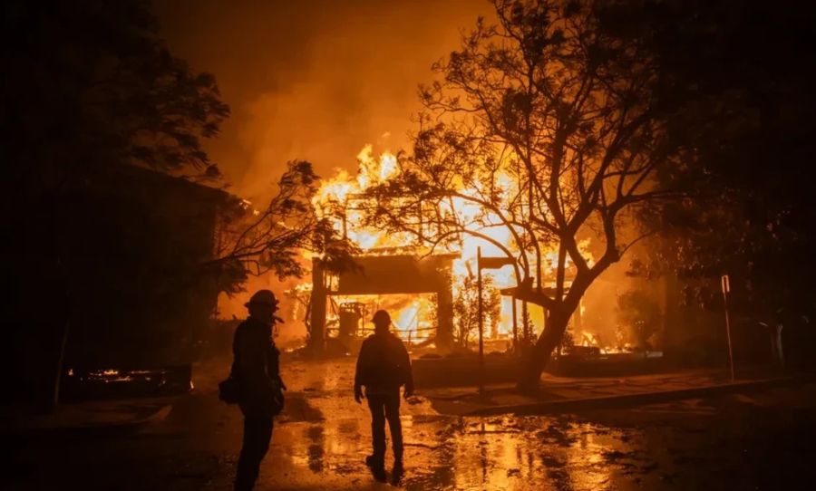 Firefighters watch the flames from the Palisades Fire burning a home during a powerful windstorm on January 8, 2025 in the Pacific Palisades neighborhood of Los Angeles.