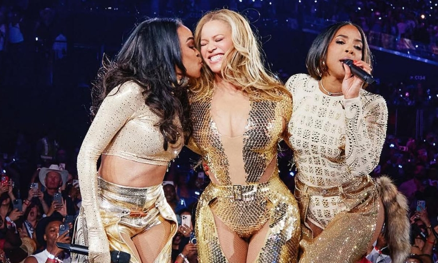 Beyoncé onstage in a gold bodysuit smiling as Michelle Williams kisses her cheek and Kelly Rowland performs, during the Destiny’s Child reunion at her Cowboy Carter tour finale in Las Vegas.