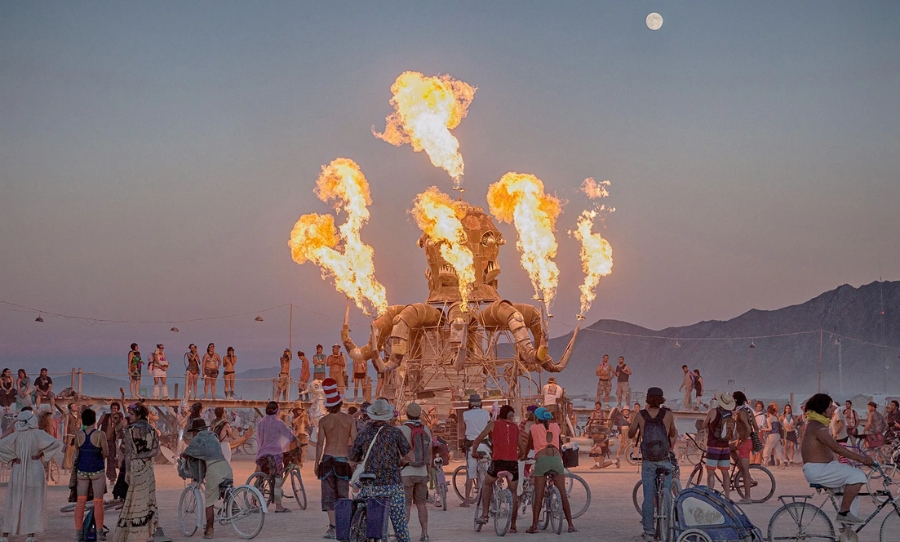 Burning Man festival attendees watch a fire-spewing art installation at sunset in Black Rock City, Nevada.