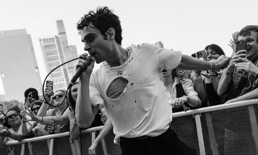 Del Water Gap performs live at Lollapalooza 2025, holding a microphone and leaning into the crowd while wearing a ripped white T-shirt.